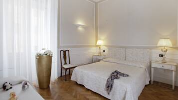 Ein Hotelzimmer mit einem großen Bett, zwei Nachttischen mit Lampen, einem Sessel, einer großen Vase mit Blumen und einem Holzboden.