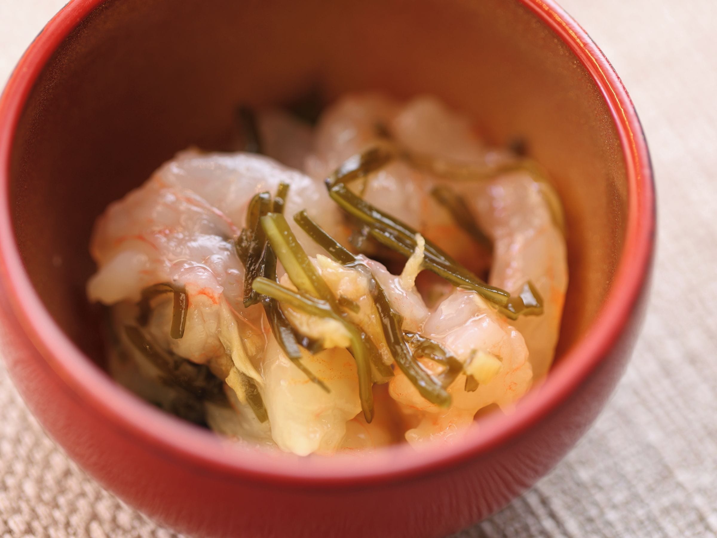 A close-up of a red bowl containing a dish with shrimp and green vegetables.