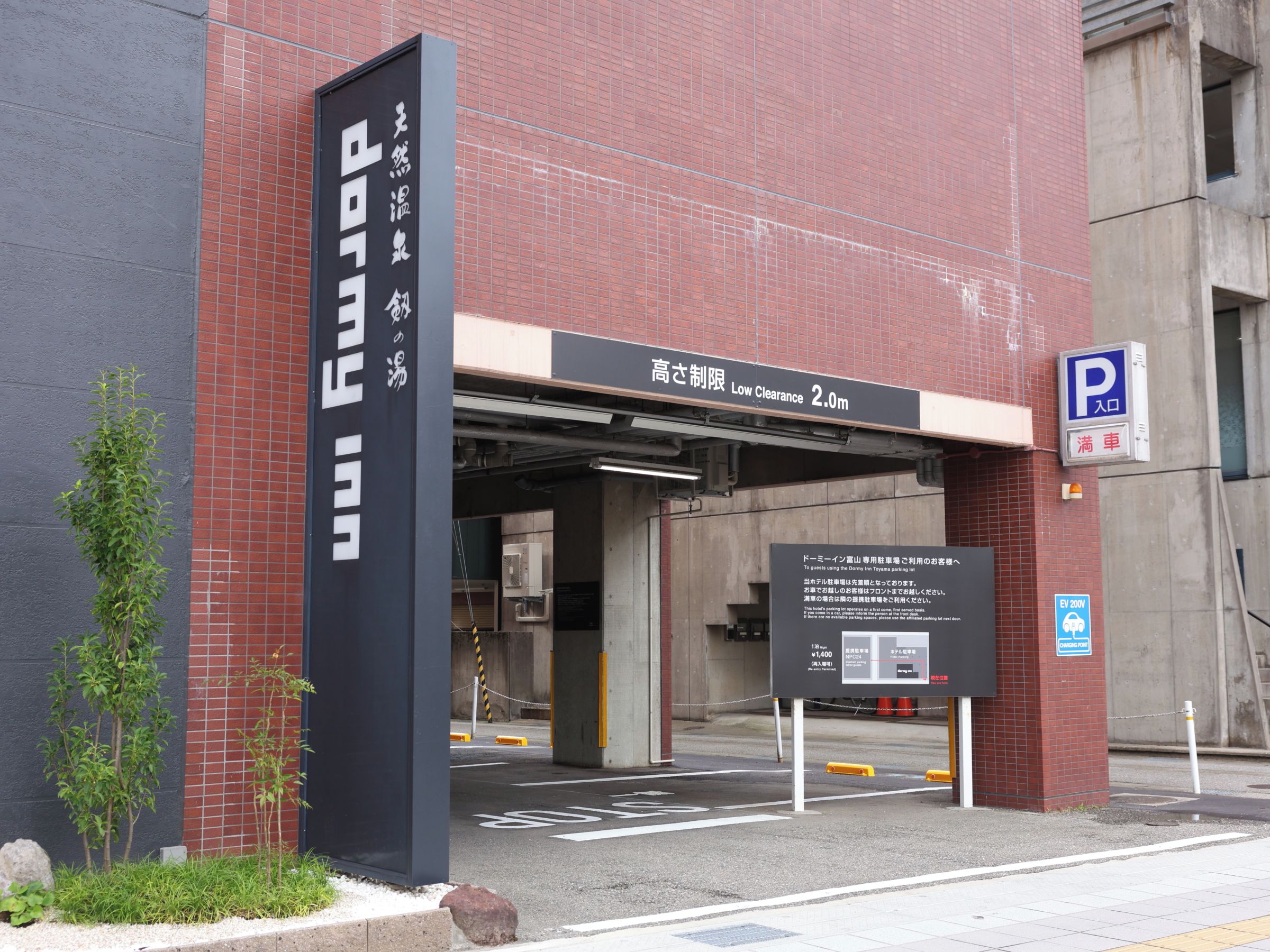 Entrada de estacionamiento con señal de altura limitada y zona reservada para vehículos eléctricos.