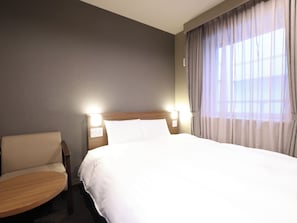 Una habitación de hotel con cama, una silla, una mesita y una ventana con cortinas.