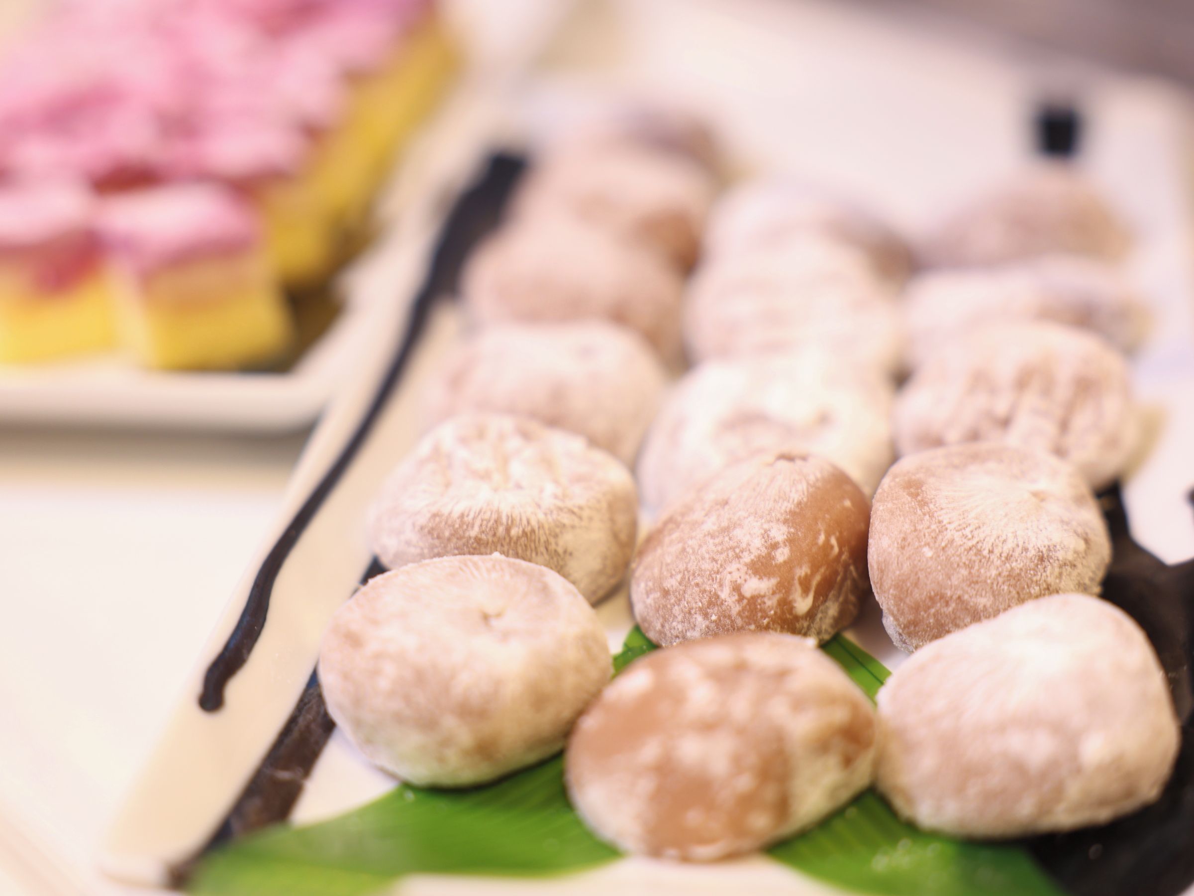 A tray of round pastries dusted with powdered sugar, arranged on a green leaf.