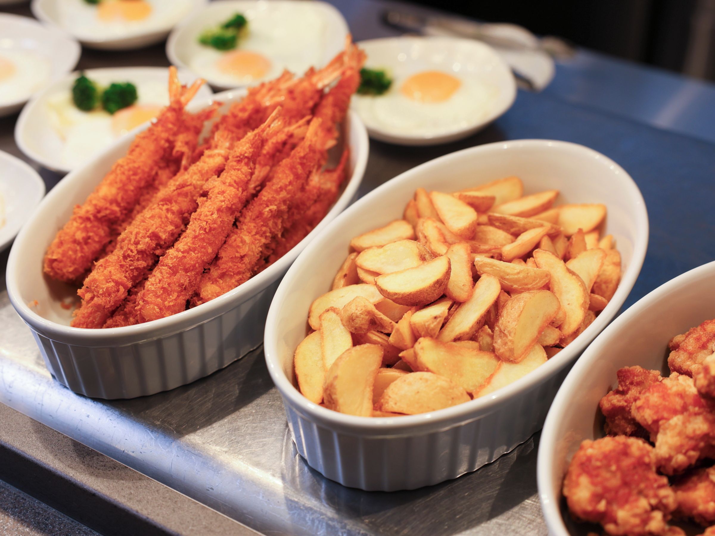 A buffet table with various dishes including fried items and potato wedges.