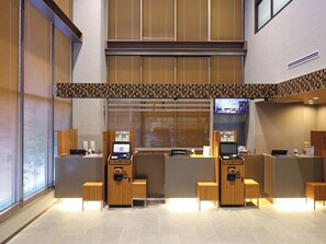 A reception area with a modern design, featuring a wooden reception desk, a digital information kiosk, and a seating area. - Dormy Inn Toyama Natural Hot Spring (Toyama)