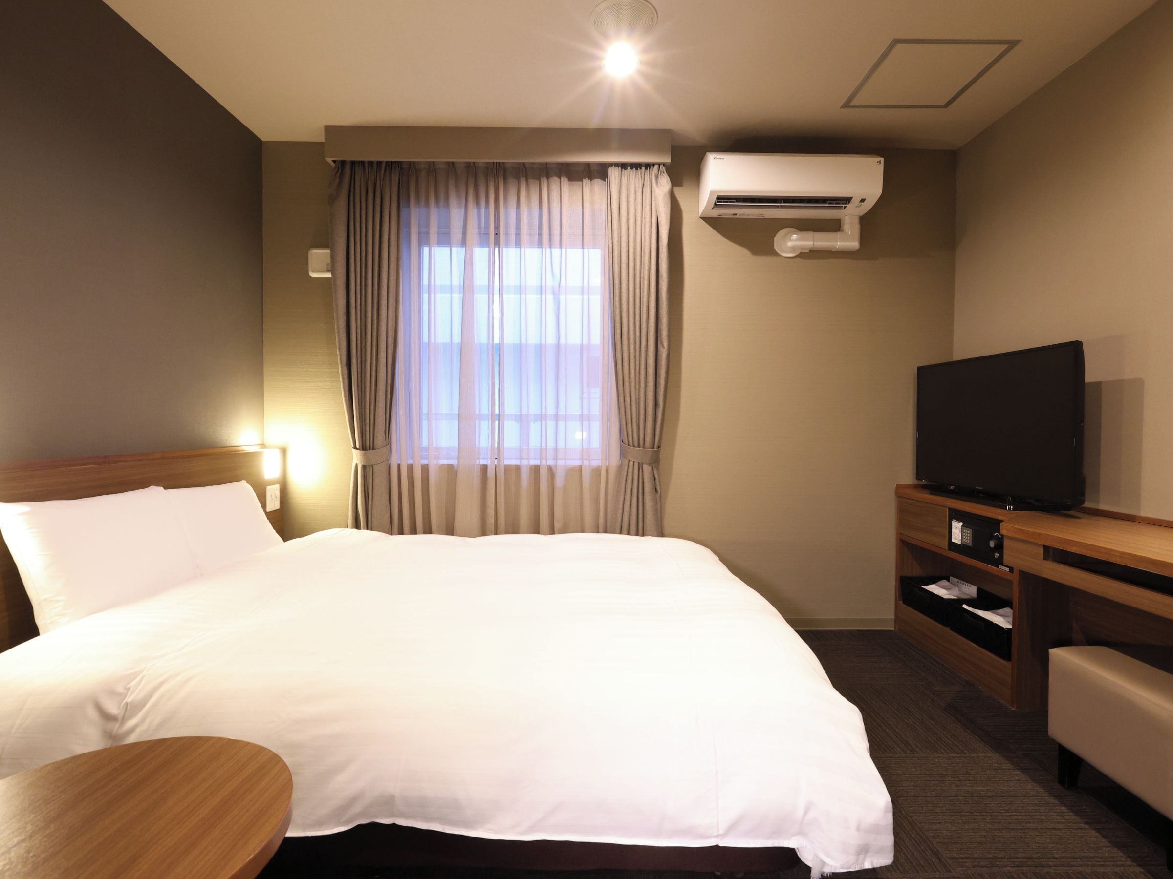 A hotel room with a bed, a television, a desk, and an air conditioning unit.