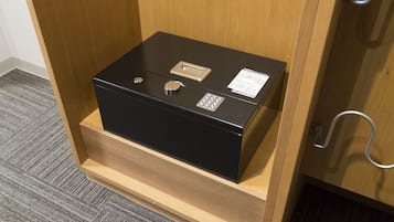 Una caja fuerte negra con asa metálica y cerradura, ubicada sobre un estante de madera dentro de un mueble de madera.