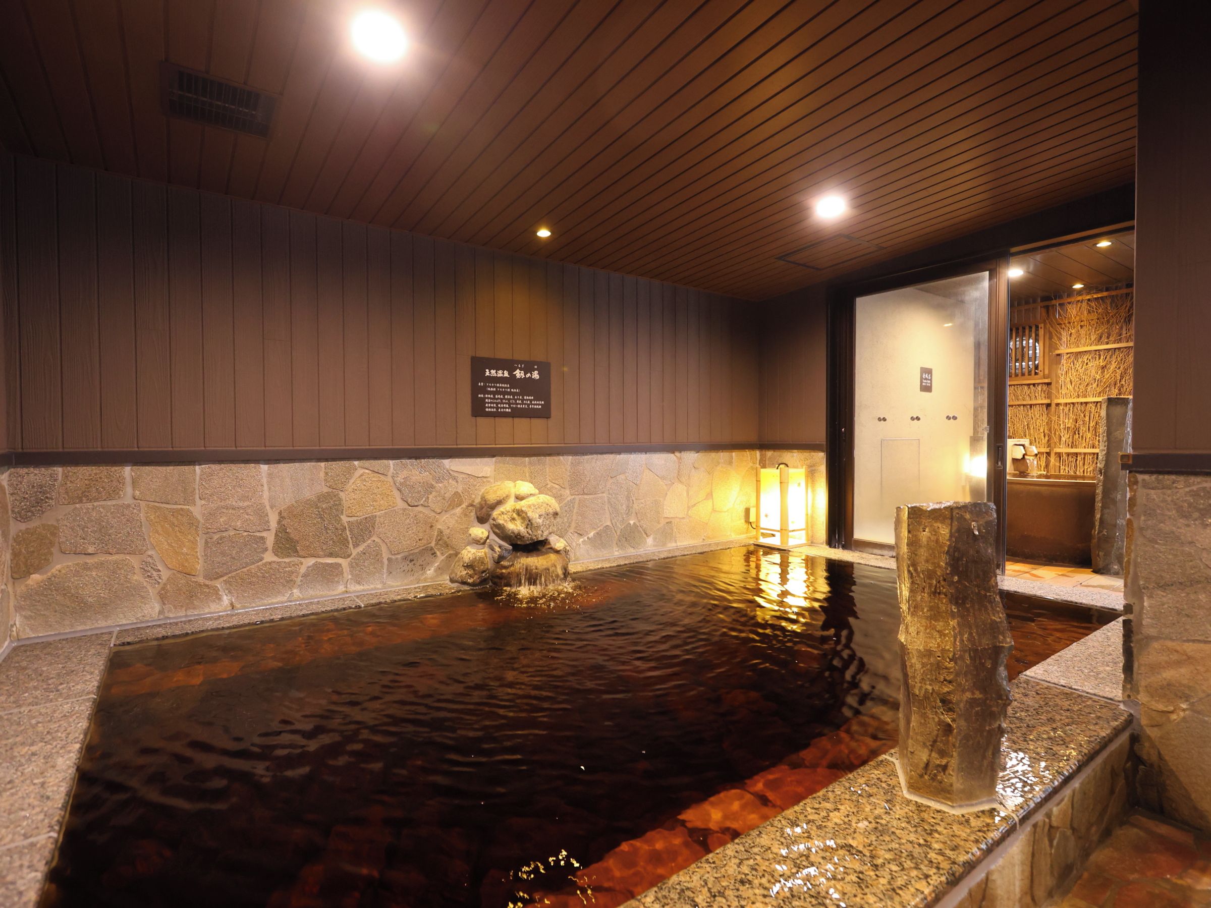 A stone hot spring with a wooden ceiling and a stone wall.