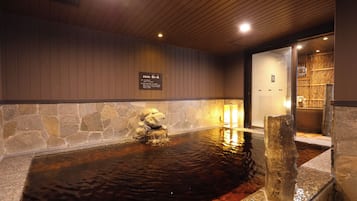 A stone hot spring with a wooden ceiling and a stone wall.