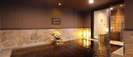 A stone hot spring with a wooden ceiling and a stone wall.