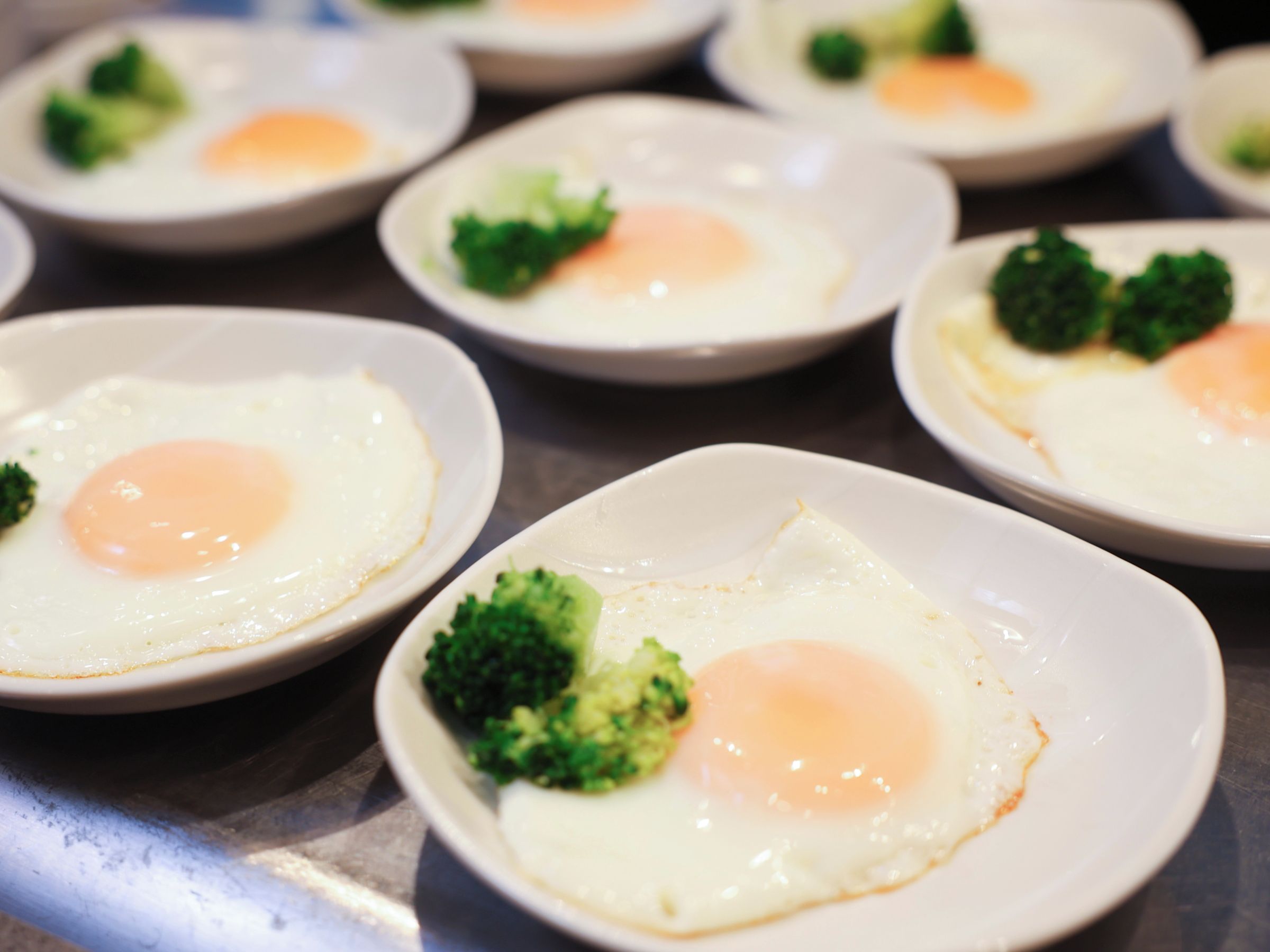 A series of white plates with fried eggs and broccoli.