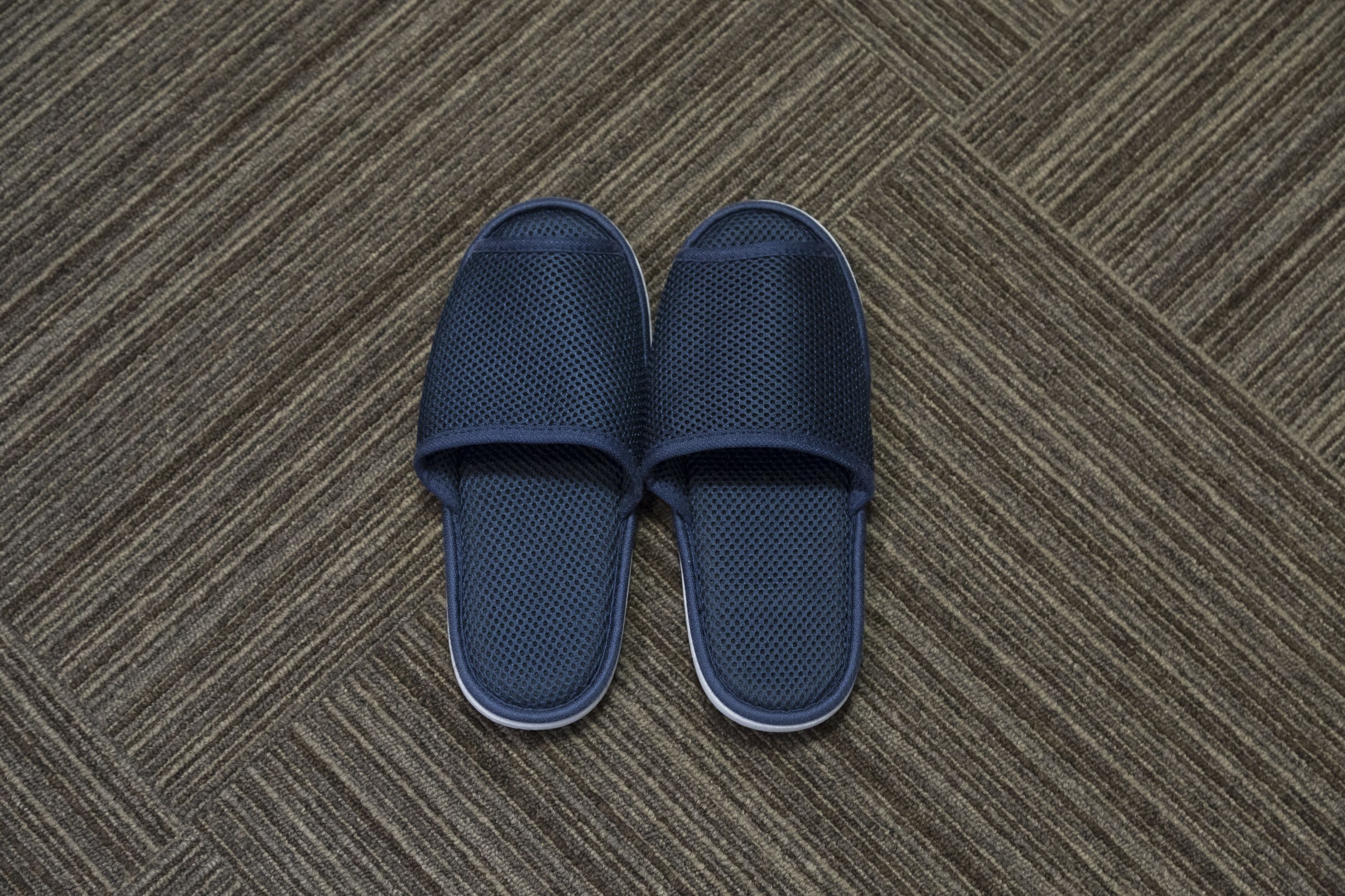 A pair of dark blue mesh slippers on a textured carpet.