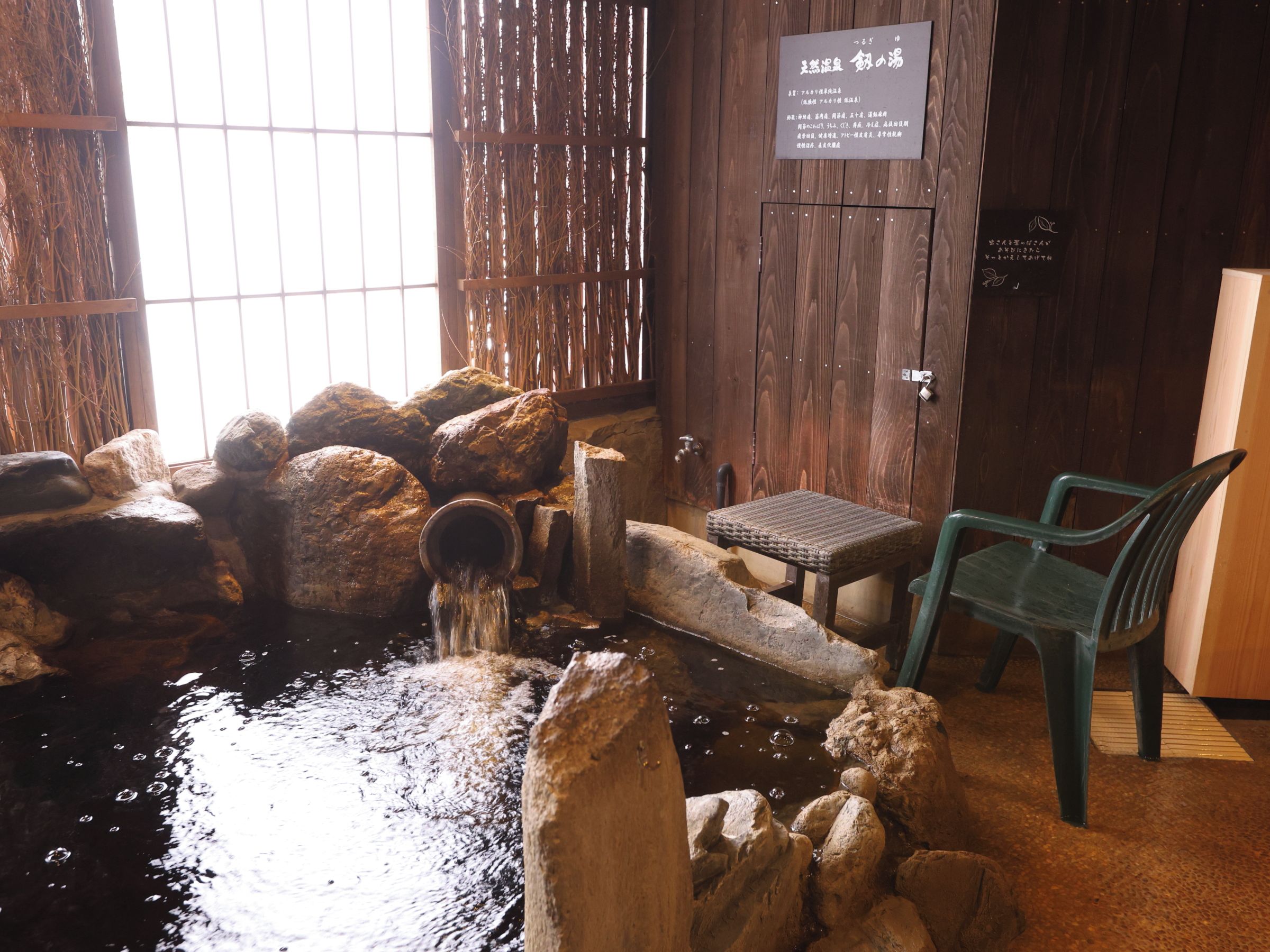 A traditional Japanese onsen with a wooden interior, a stone hot spring, and a wooden bench.