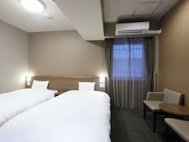 A hotel room with two beds, a desk, a chair, an air conditioning unit, and a window with curtains.