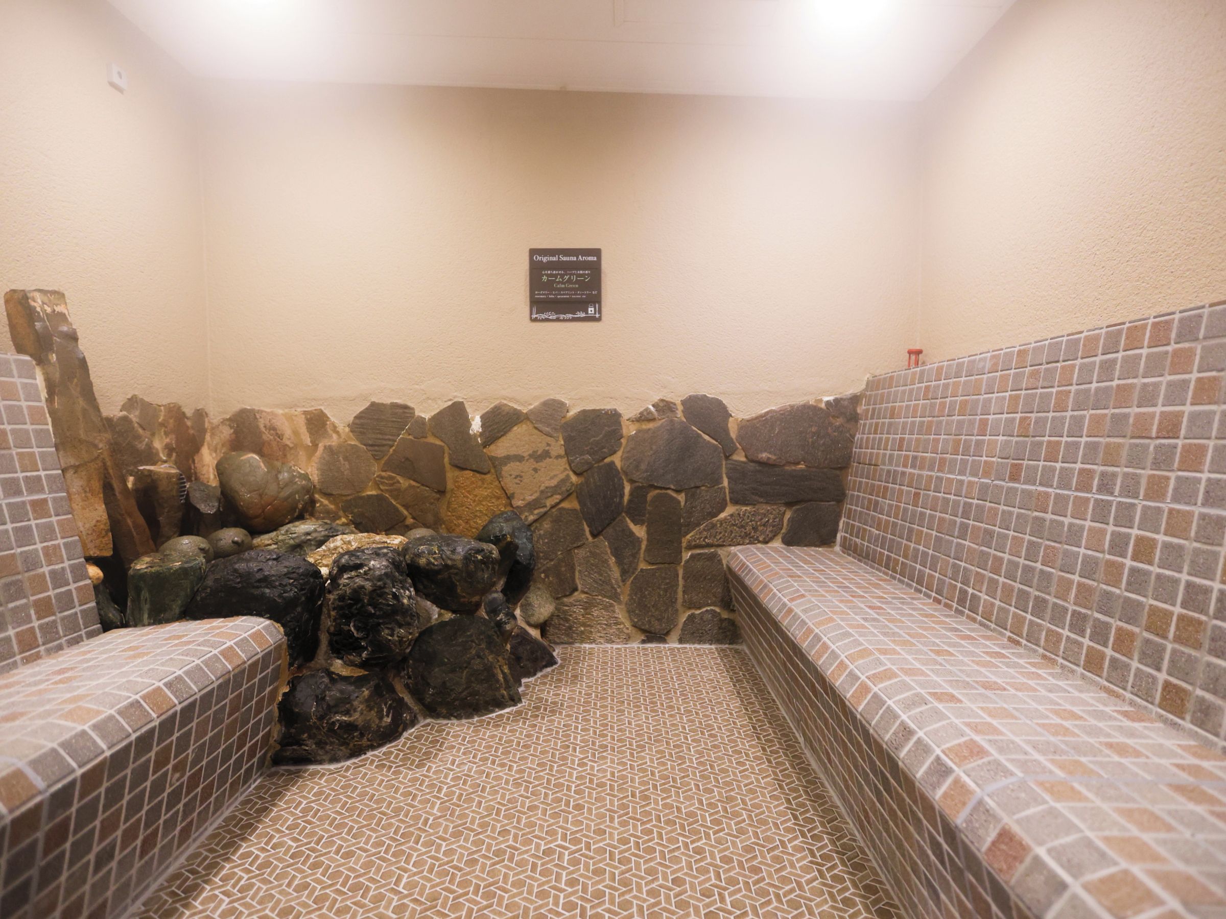 A sauna with tiled walls and benches, a stone wall, and a sign indicating the original sauna aroma.