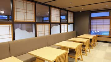 A restaurant interior with wooden tables and benches, large windows with traditional paper screens, and a view of the outside.