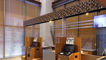 A modern hotel reception area with wooden reception desks, a digital information screen, and a view of the outside through large windows.
