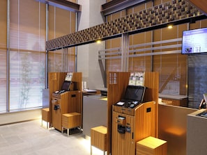 A modern hotel reception area with wooden reception desks, a digital information screen, and a view of the outside through large windows. - Dormy Inn Toyama Natural Hot Spring (Toyama)