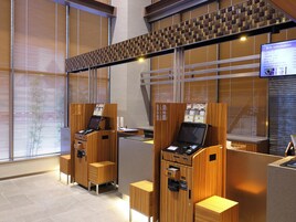Una moderna area reception di un hotel, con scrivanie in legno, uno schermo digitale informativo e vista all'esterno attraverso ampie vetrate.