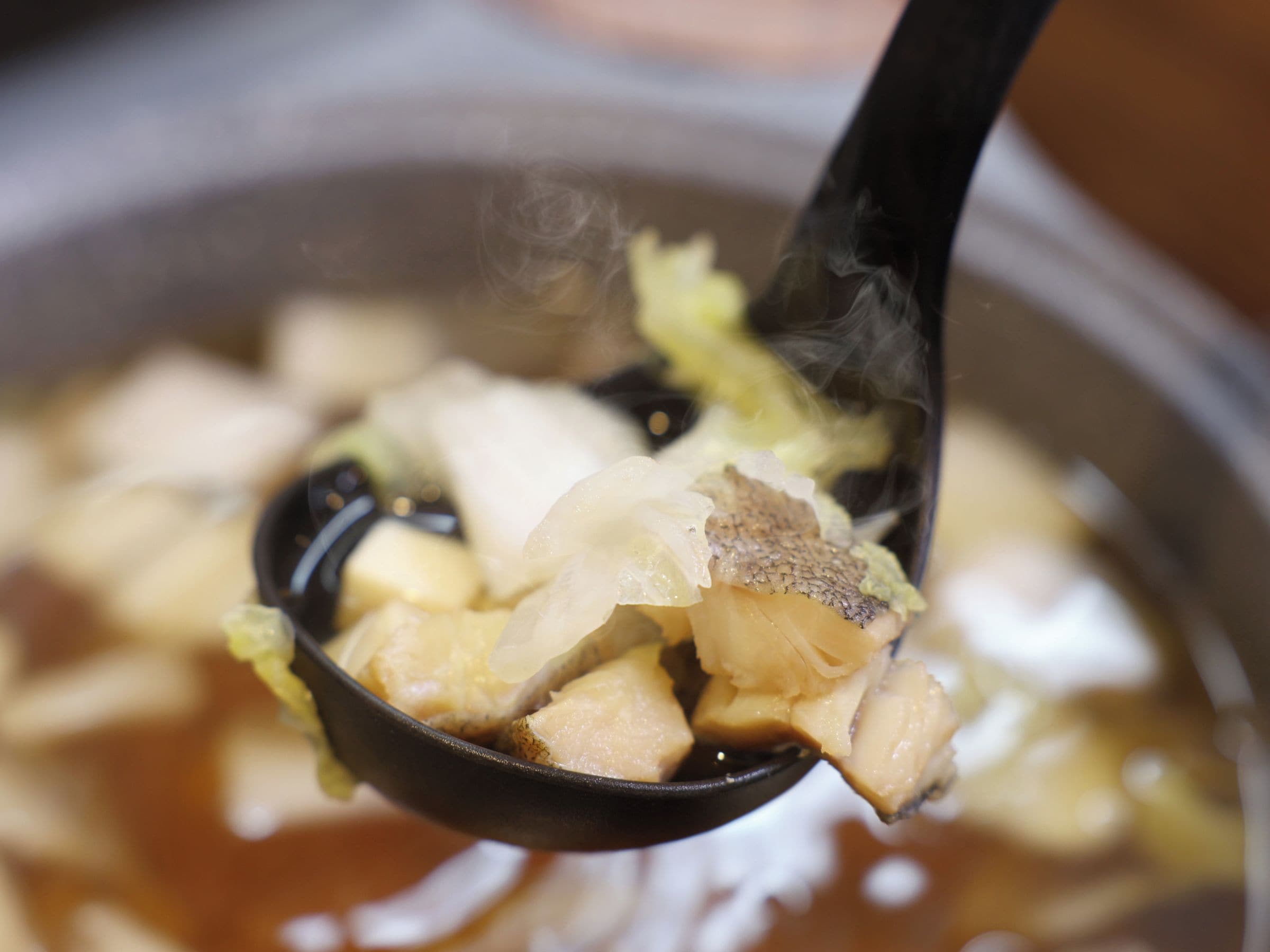 A close-up of a spoon lifting food from a pot.