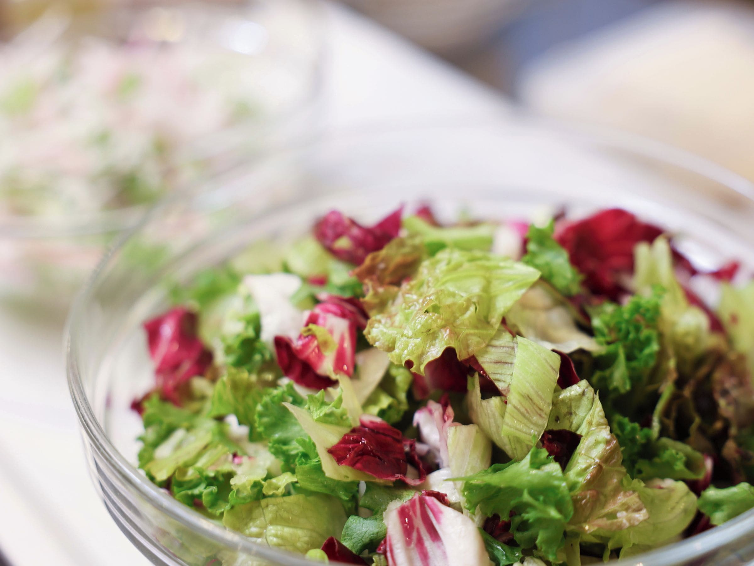 A clear glass bowl filled with a salad of mixed greens and red leaves, likely containing lettuce and radicchio.