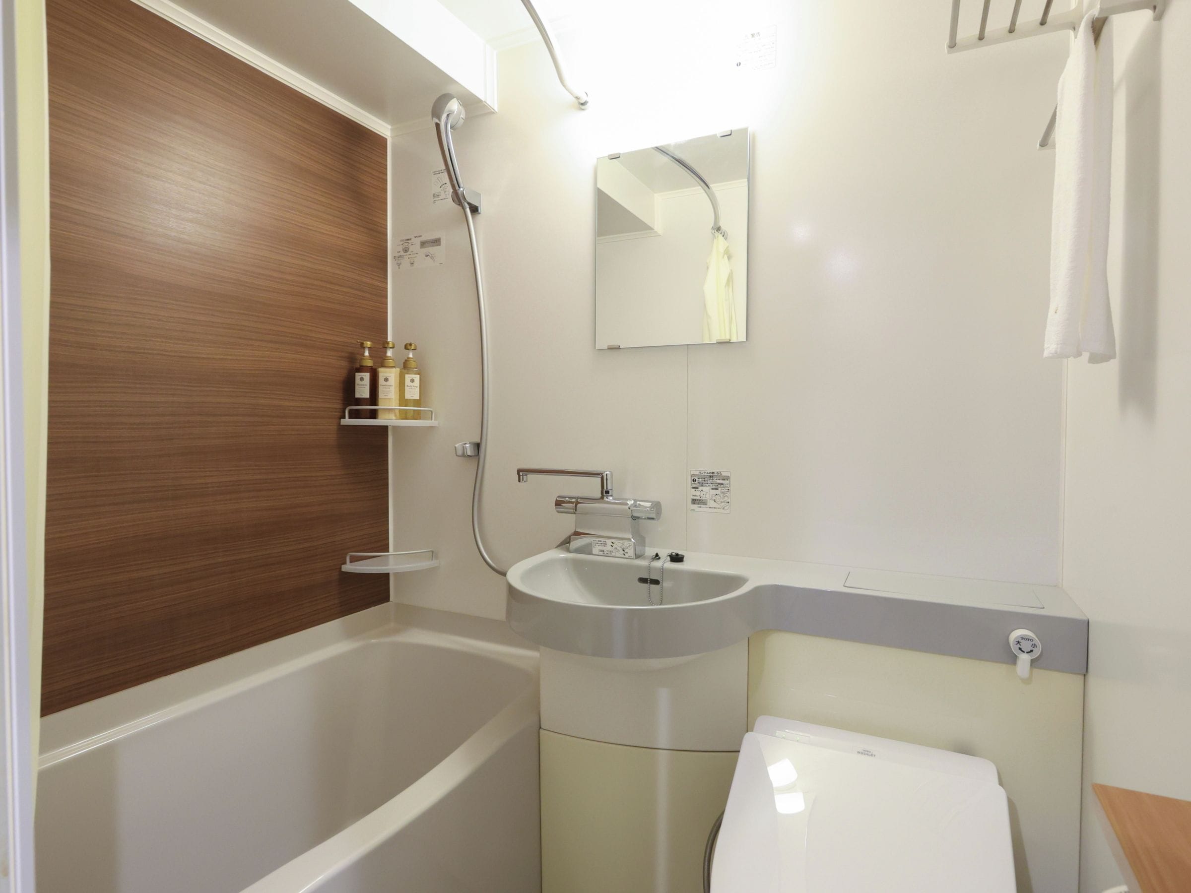 A bathroom with a bathtub, sink, and toilet. There are toiletries on a shelf and a towel hanging on a rack.