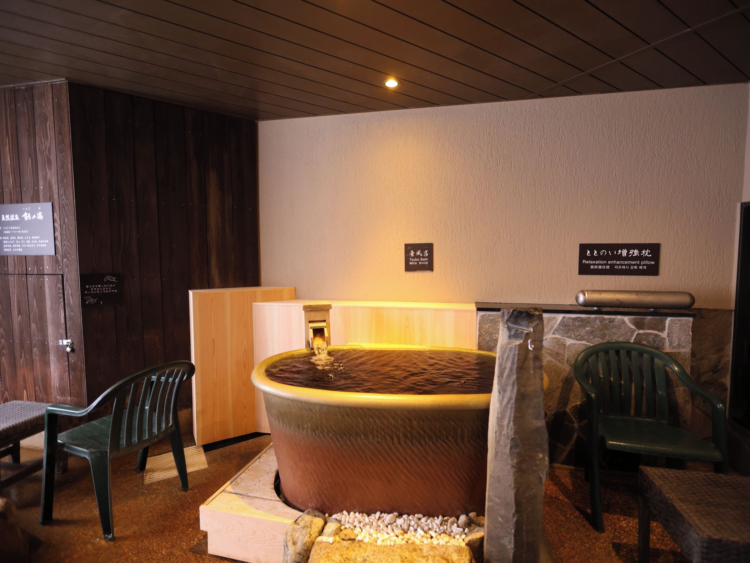 Une salle de spa avec un jacuzzi, des murs en bois et deux fauteuils verts.