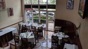 A restaurant with multiple tables and chairs, large windows with a view of parked cars and greenery outside. - Hotel Del Principado (Mexico City)
