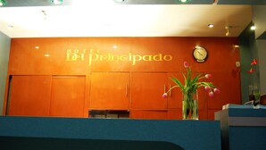 A hotel reception area with a clock and a vase of flowers. - Hotel Del Principado (Mexico City)