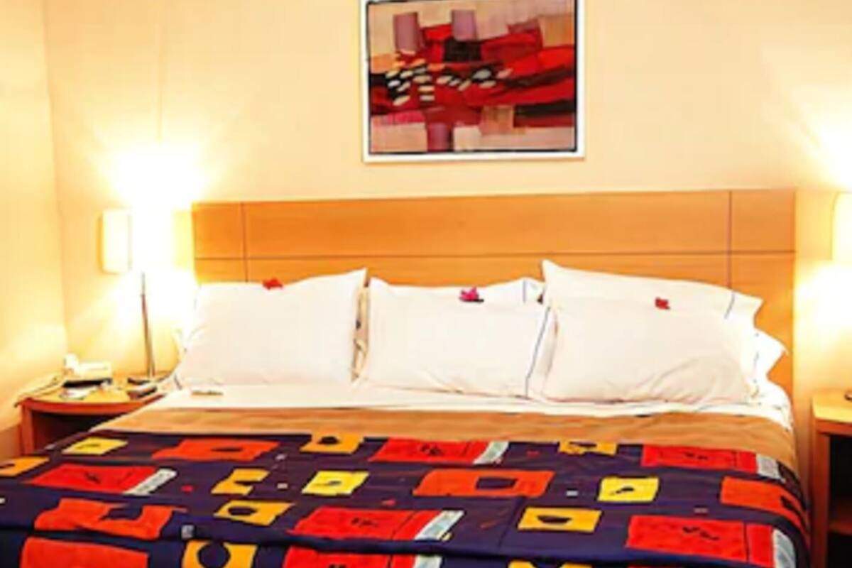 Quarto de hotel com uma cama, duas mesas de cabeceira e um quadro na parede.