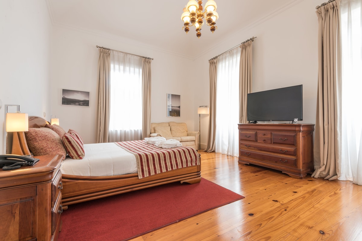A spacious bedroom with a large bed, a wooden dresser, a television, and a red rug.