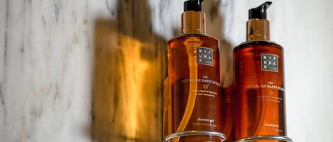 Two bottles of Ritual of Happy Buddies shower gel and shampoo on a marble surface.
