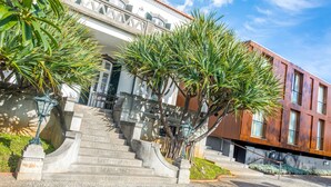 A modern building with a staircase leading to a balcony, surrounded by palm trees.