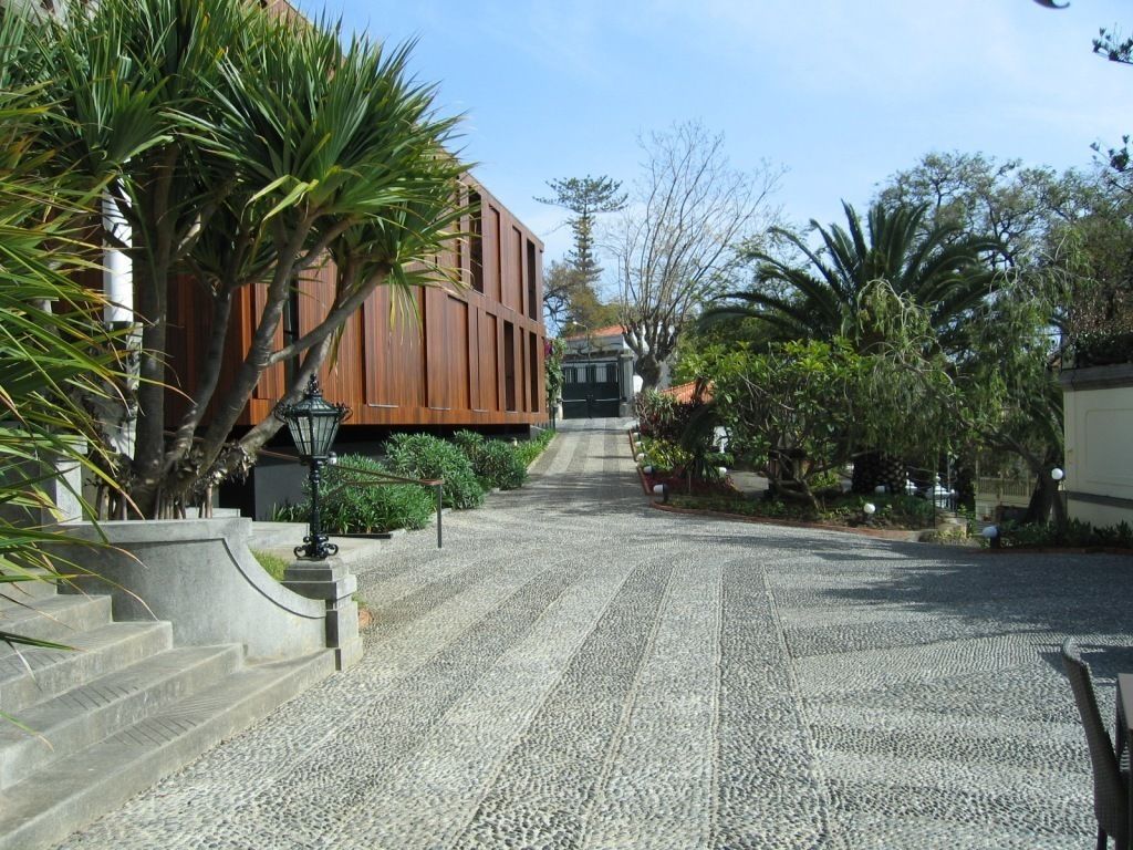 A paved pathway leading to a building with a modern design, surrounded by lush greenery and a clear sky.