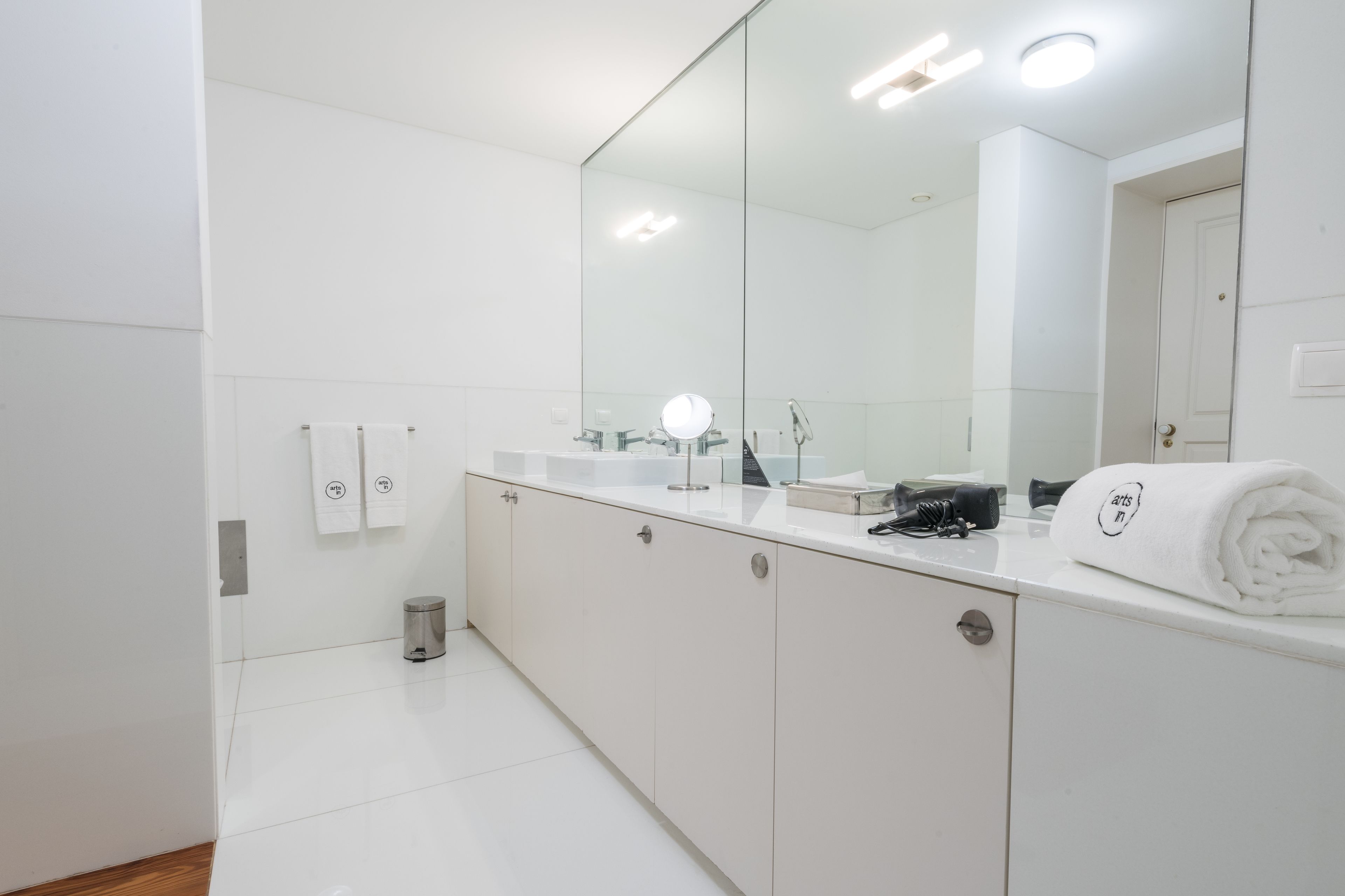 Une salle de bain moderne avec un grand miroir, des meubles blancs et une serviette posée sur le comptoir.