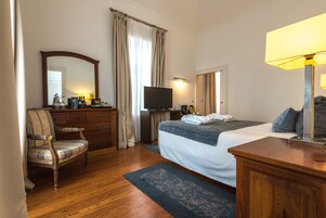 A hotel room with a bed, a desk, a chair, a television, and a lamp.