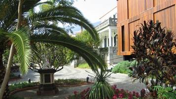 A courtyard with a statue, palm trees, and a building with wooden panels.