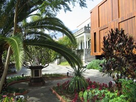 A courtyard with a statue, palm trees, and a building with wooden panels.