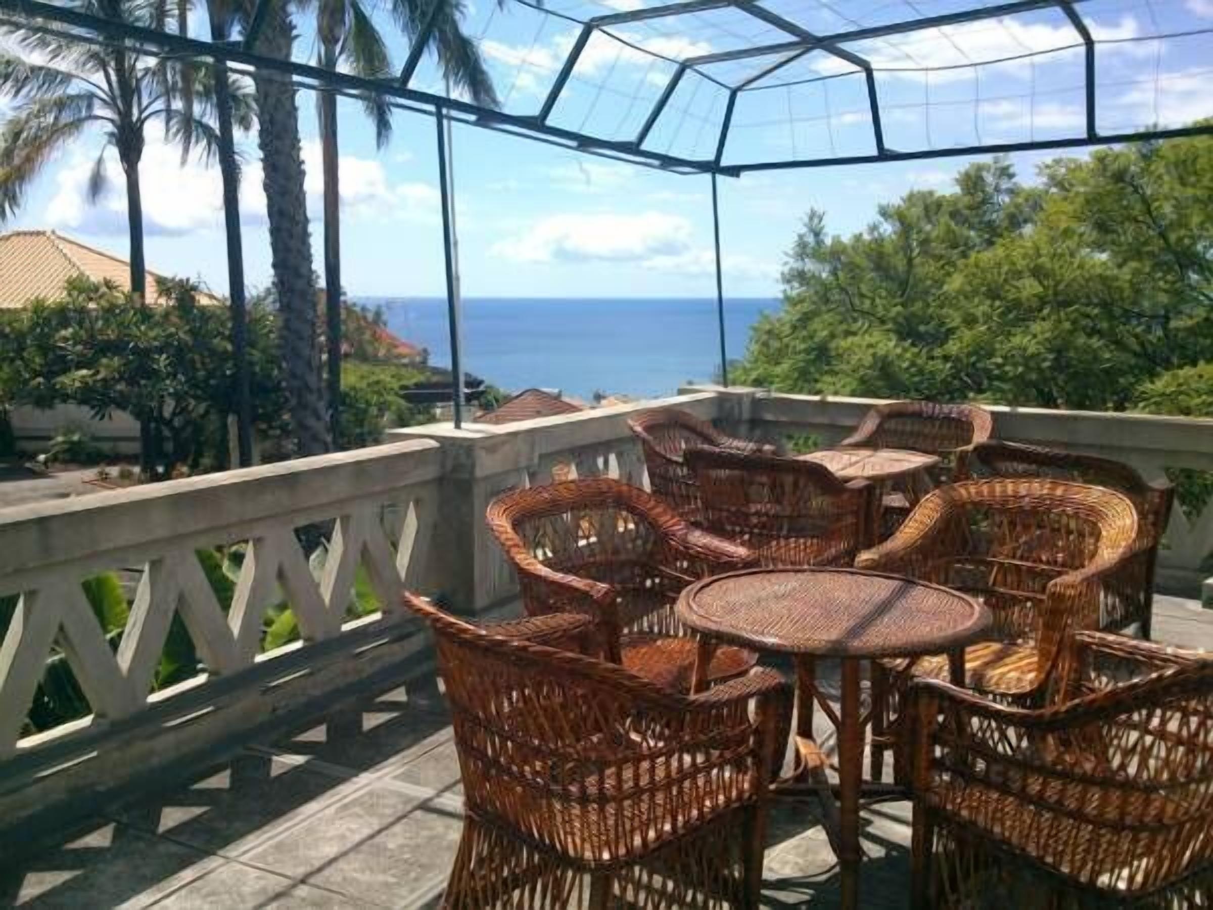 A covered outdoor seating area with wicker furniture and a view of the ocean.