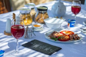 A table set with a menu, a glass of red wine, a plate of food including sausages and tomatoes, and various condiments and jars. - Arts In Hotel Conde Carvalhal (Funchal)
