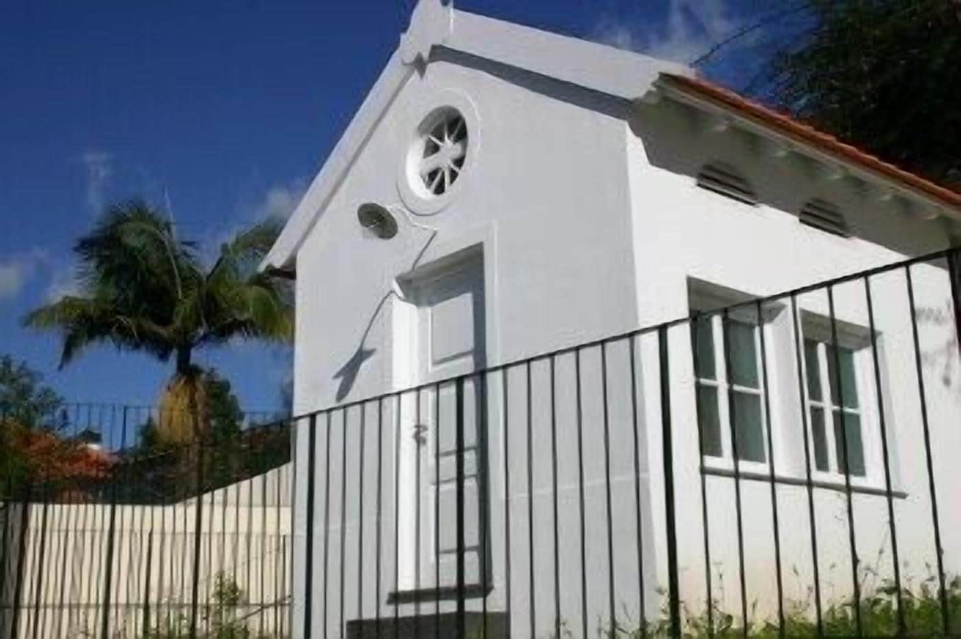 A white building with a circular window and a door, surrounded by a black metal fence.