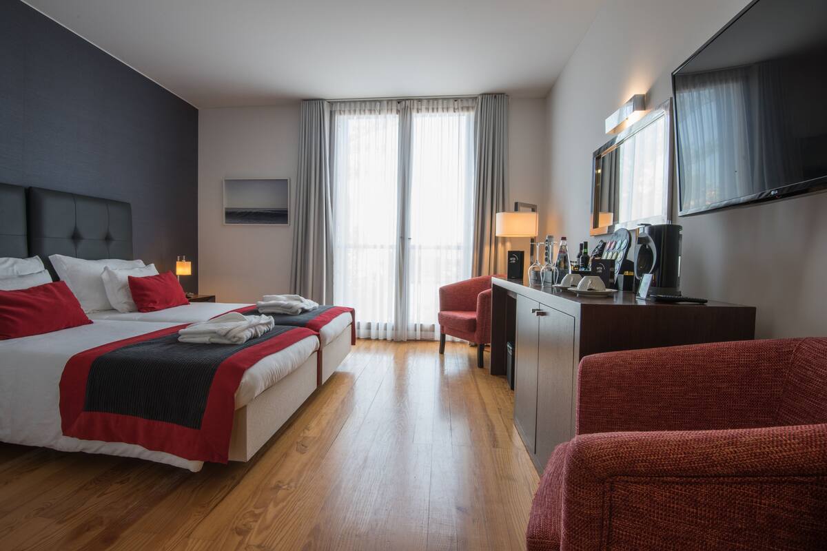Habitación de hotel con dos camas, un escritorio, una silla, un televisor y una ventana con cortinas.