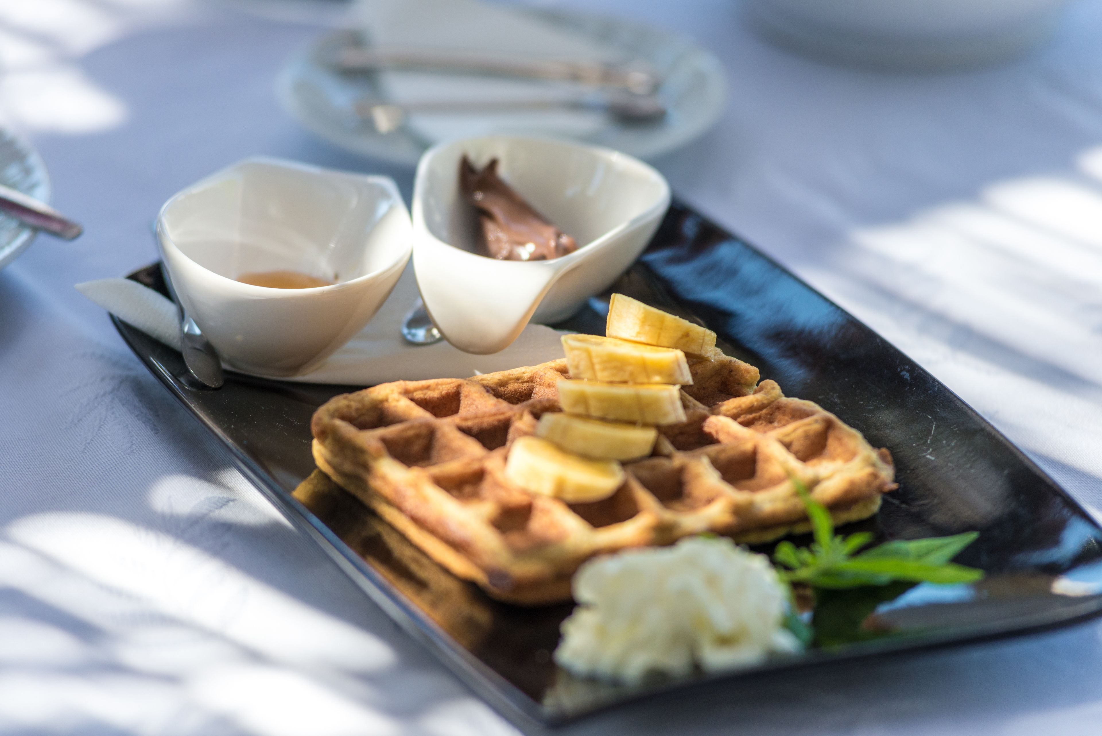 A plate with waffles, banana slices, whipped cream, and a small bowl of chocolate sauce.