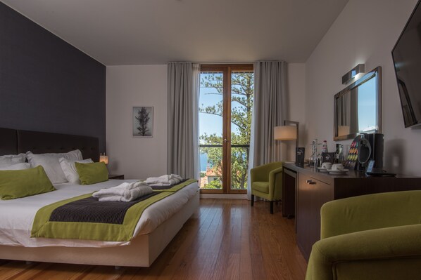 Una habitación de hotel moderna con una cama grande, un escritorio con una silla, un balcón con vistas y un espejo amplio.