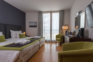 Habitación de hotel con una cama grande, un escritorio con silla, un televisor y una ventana con cortinas.