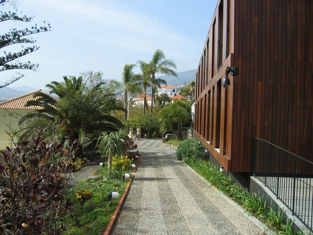 A pathway leading to a building with a wooden facade, surrounded by lush greenery and palm trees.
