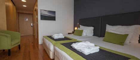 A hotel room with two beds, a green armchair, a wooden floor, and a painting on the wall.