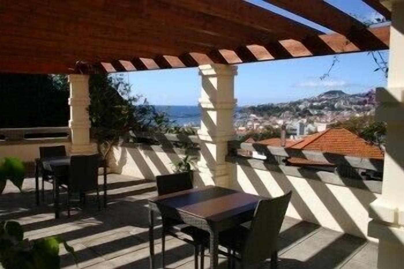 Un espace extérieur abrité, doté de tables et de chaises, offrant une vue sur une ville côtière.