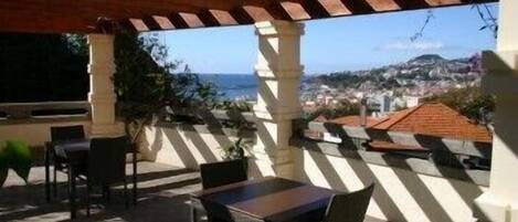 A covered outdoor seating area with tables and chairs, overlooking a coastal town.