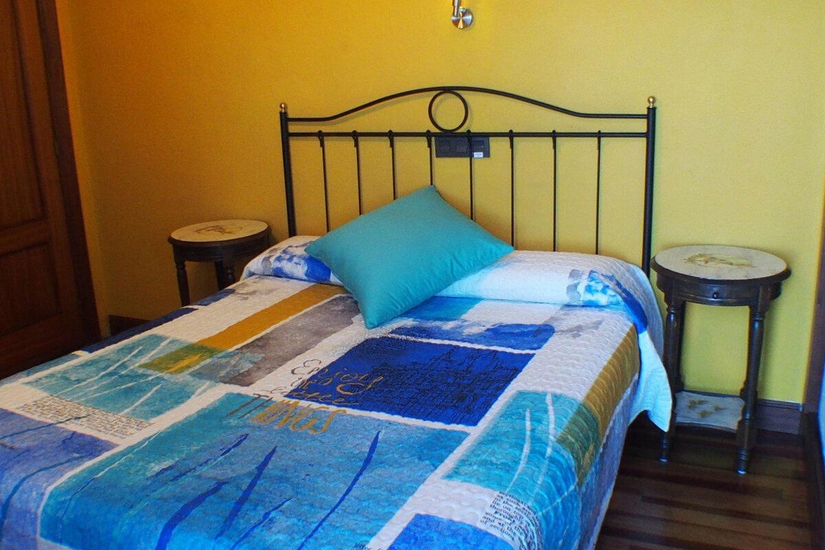 A bed with a quilt, two bedside tables, and a wall-mounted light fixture.