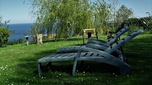 A grassy area with two lounge chairs and a wooden bench, overlooking a body of water. - Casa Rural Arboliz (Ibarranguelua)