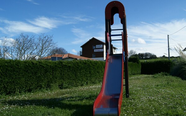 A red slide in a grassy area with a house in the background. - Casa Rural Arboliz (Ibarranguelua)